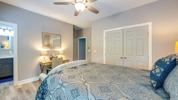 A bedroom with a patterned bedspread, a ceiling fan, a bedside table with a lamp, a dresser, and a mirror.