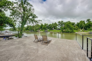 A concrete deck with two metal chairs overlooking a body of water, surrounded by trees and a grassy area. - Outdoor Entertainment Space: Home in Mcqueeney (McQueeney)