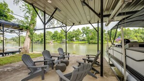 Un espace extérieur aménagé avec des chaises Adirondack et une table, offrant une vue sur un plan d’eau et un quai où est amarré un bateau.