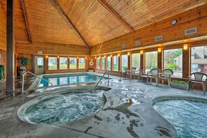 Un área de piscina interior con dos jacuzzis, techo de madera y ventanas amplias.