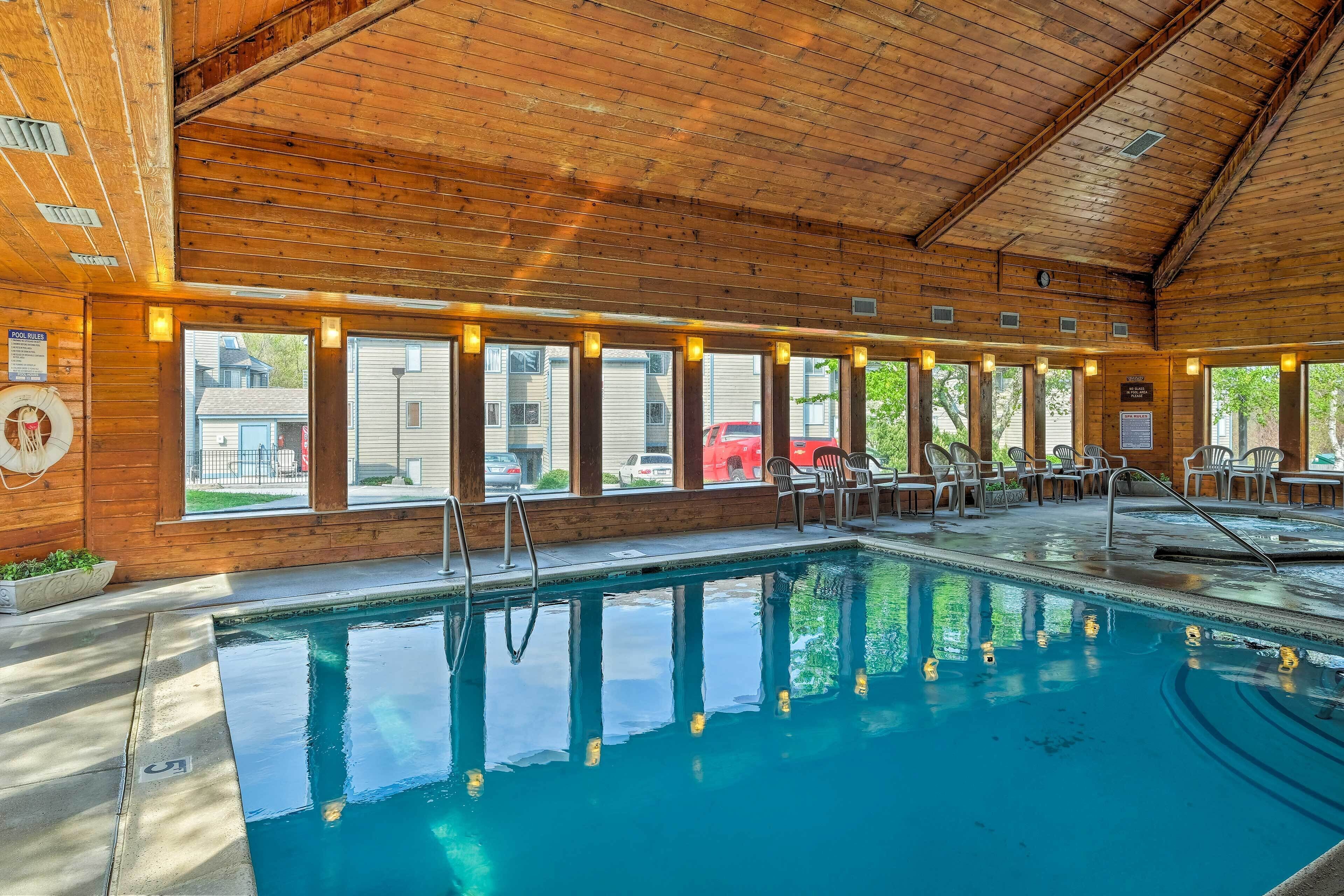 Un espace intérieur avec piscine, dont les murs sont recouverts de panneaux de bois, doté de grandes fenêtres, d’un poste de surveillance pour le sauveteur et d’un escalier pour accéder à la piscine.