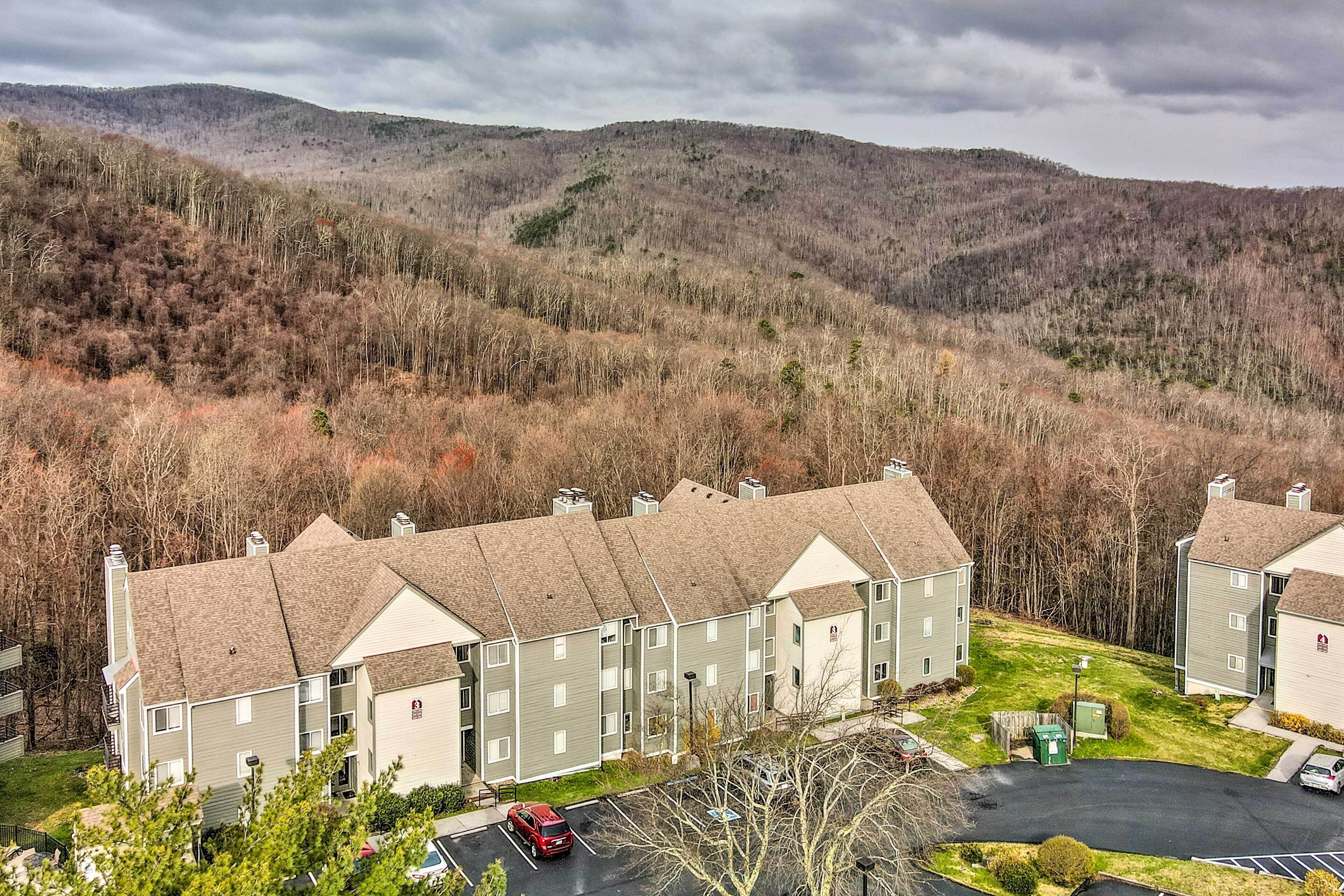 A multi-story residential building with a parking area and a view of a forested hillside.