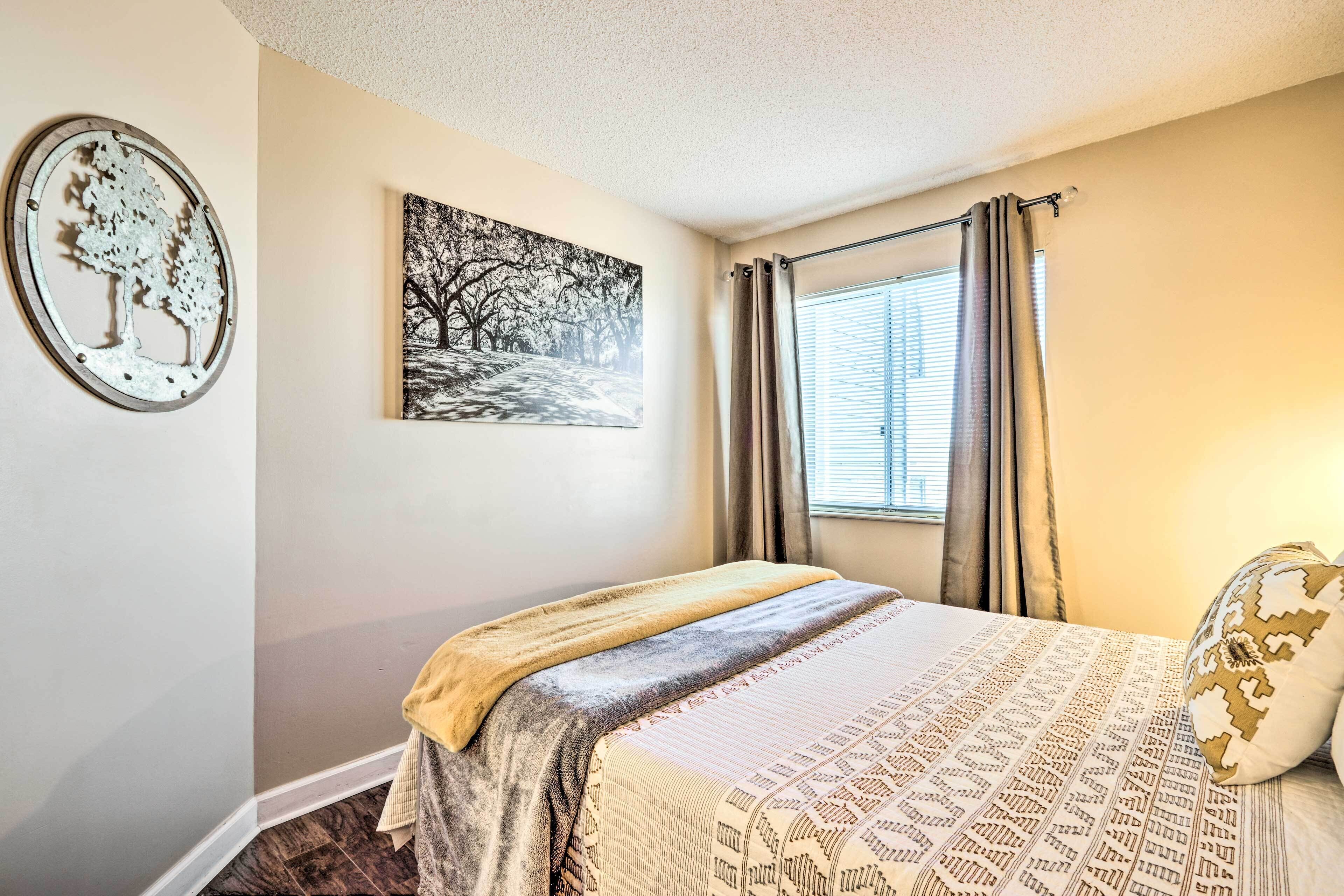 A bedroom with a bed, a window with curtains, a wall-mounted artwork, and a decorative metal piece.