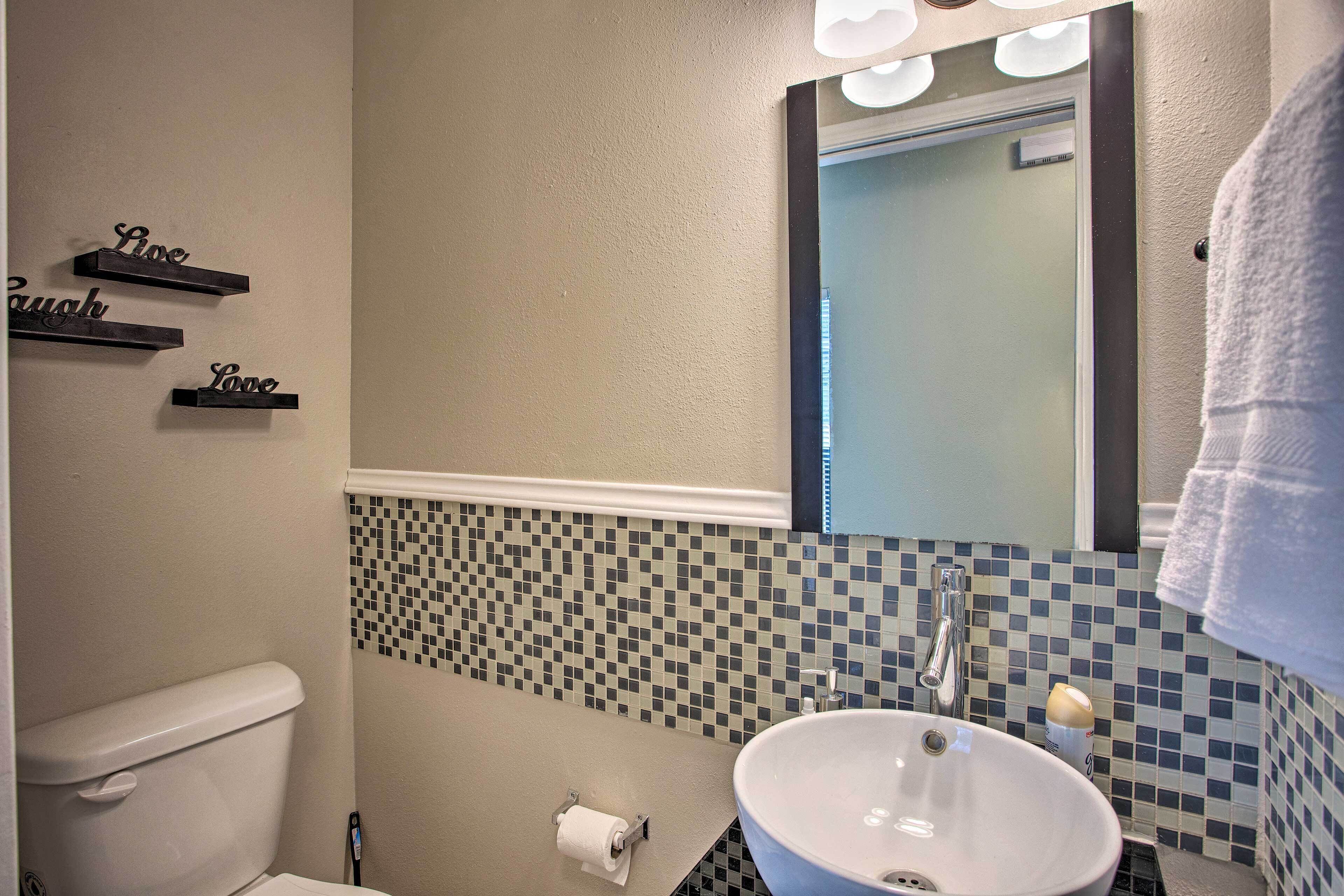 A bathroom with a toilet, a sink, and a mirror. There are three signs on the wall with the words "Love," "Laugh," and "Live."
