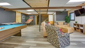A pool table, a sofa, a television, and a staircase in a room with wooden flooring and a sloped ceiling. - Spacious Wellston Home Near Hiking & Skiing! (Wellston)