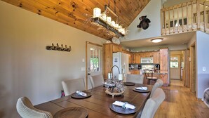 A dining area with a wooden table set for four, surrounded by cushioned chairs. A chandelier hangs from the ceiling, and a bear decoration is visible on the wall. - Game Room & Fire Pit: Picturesque Cabin in Murphy (Murphy)
