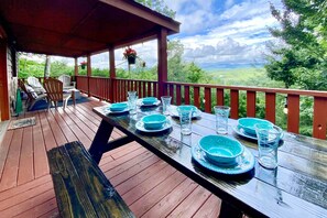 Une terrasse en bois avec une table dressée pour quatre personnes, offrant une vue sur un paysage magnifique.