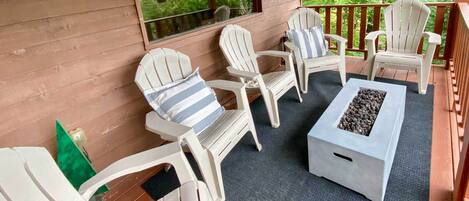 Ein überdachter Außenbereich mit Adirondack-Stühlen und einem Feuerkorb.