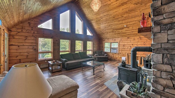 A spacious log cabin interior with a large fireplace, multiple seating areas, and large windows offering natural light and views. - Cozy Family-friendly Pine Grove Cabin w/ Fire Pit! (Pine Grove)