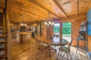 A wooden cabin interior with a dining area, kitchen, and a large window overlooking greenery. - Cozy Family-friendly Pine Grove Cabin w/ Fire Pit! (Pine Grove)