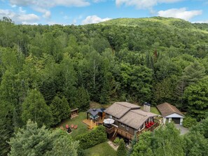 A two-story house with a deck, surrounded by dense forest.