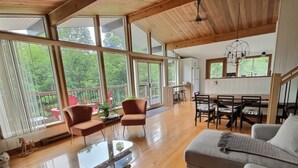 A spacious living area with large windows, a wooden ceiling, and a dining area with a table and chairs.