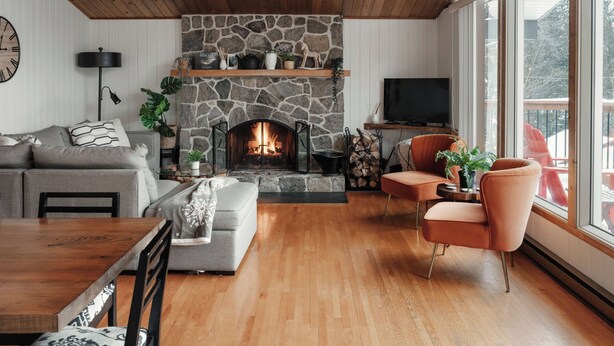 A cozy living room with a stone fireplace, wooden ceiling, and large windows.