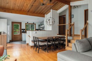 A spacious living area with a wooden dining table, a sofa, and a staircase leading to an upper level.