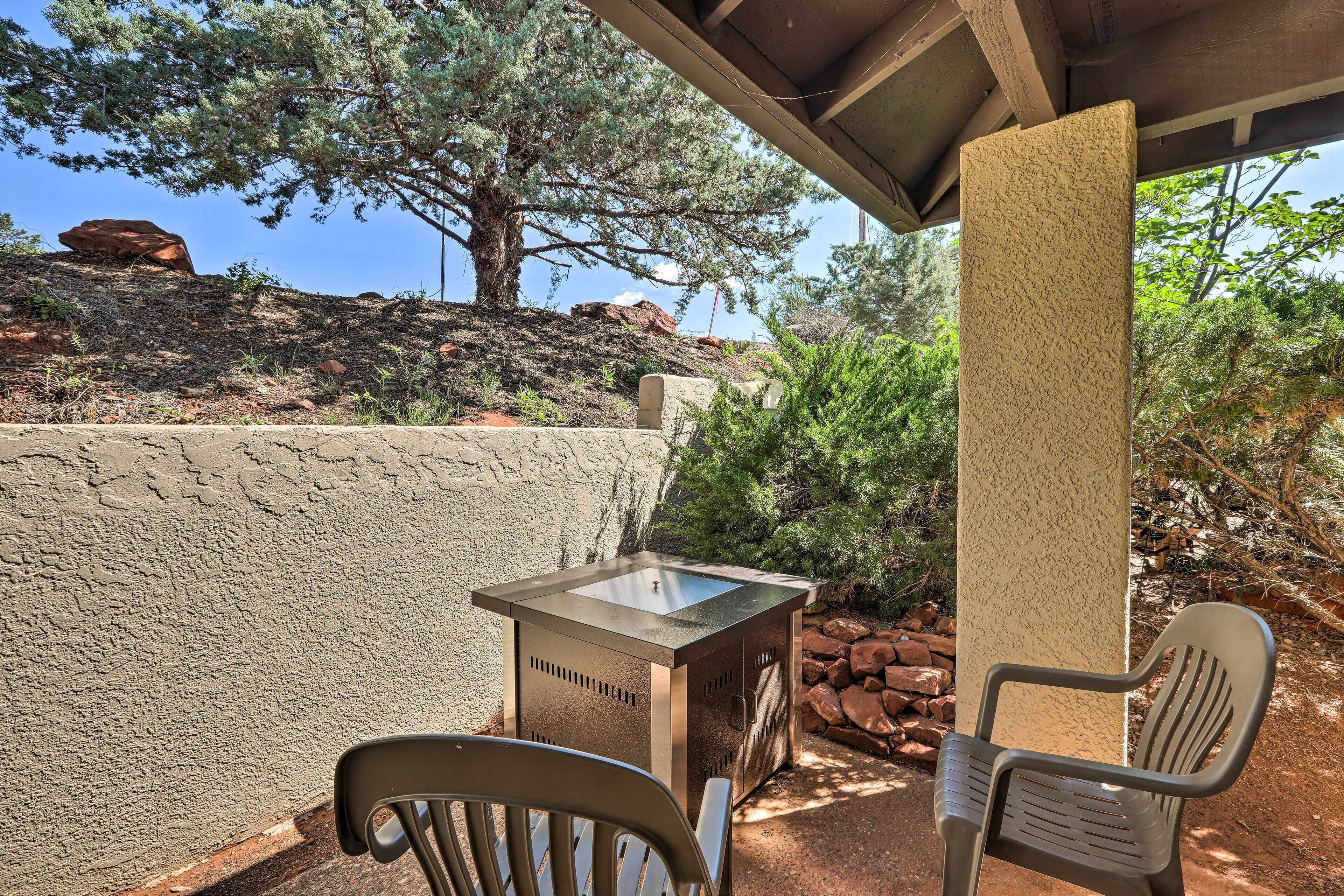 An outdoor patio with a stone table and two chairs, surrounded by natural scenery and a clear sky.