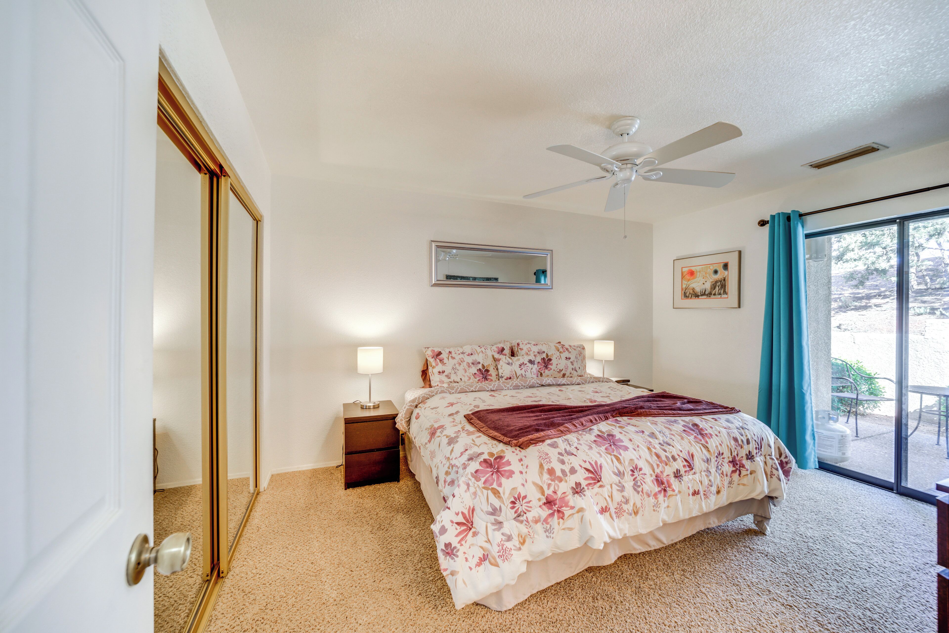 A bedroom with a bed, bedside lamps, a ceiling fan, a window with curtains, and a door.
