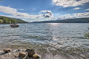 Um lago calmo com um barco atracado à esquerda, rodeado por margens rochosas e colinas ao fundo.