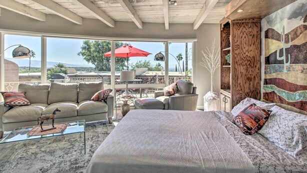 A spacious bedroom with a large bed, a seating area with a sofa and chairs, and a view of the outdoors through large windows. - Near Golf: Mtn-view Studio in Tucson! (Tucson)