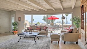 A spacious living room with a large window, a ceiling with exposed beams, a sofa set, a coffee table, and a potted plant. - Near Golf: Mtn-view Studio in Tucson! (Tucson)