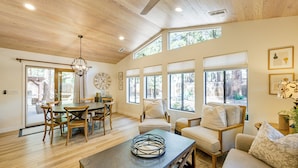 Un amplio espacio habitable con techo de madera, ventanas grandes, una mesa de comedor y asientos cómodos.