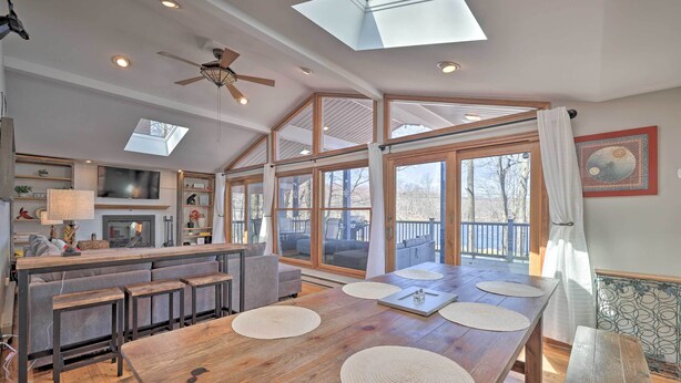 A spacious kitchen with a large island, a dining area with a wooden table and benches, and large windows offering a view of the outdoors. - Locust Lake Village Cabin w/ Deck & Lake View! (Pocono Lake)
