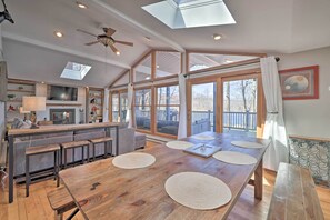 A spacious kitchen with a large island, a dining area with a wooden table and benches, and large windows offering a view of the outdoors.