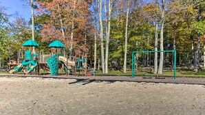 A playground with slides and climbing structures, surrounded by trees and picnic tables. - Locust Lake Village Cabin w/ Deck & Lake View! (Pocono Lake)