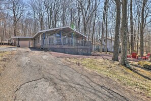 A cabin with a covered porch, a garage, and a dirt driveway.