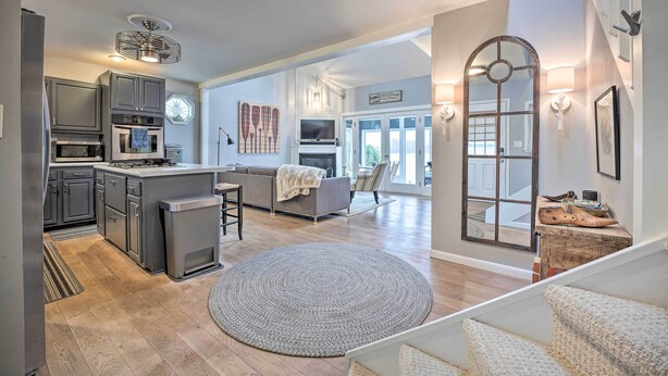 A modern kitchen with a central island, a dining area with a sofa, and a staircase leading to an upper level. - Waterfront Cable Lake Cabin w/ Grill! (Dowagiac)