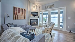 A modern living room with a fireplace, a large window, and a view of the outdoors. - Waterfront Cable Lake Cabin w/ Grill! (Dowagiac)