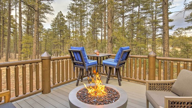 A deck with a fire pit, two chairs with blue cushions, and a view of a forest. - Torreon Cabin Escape - Relax, Recharge and Explore (Show Low)