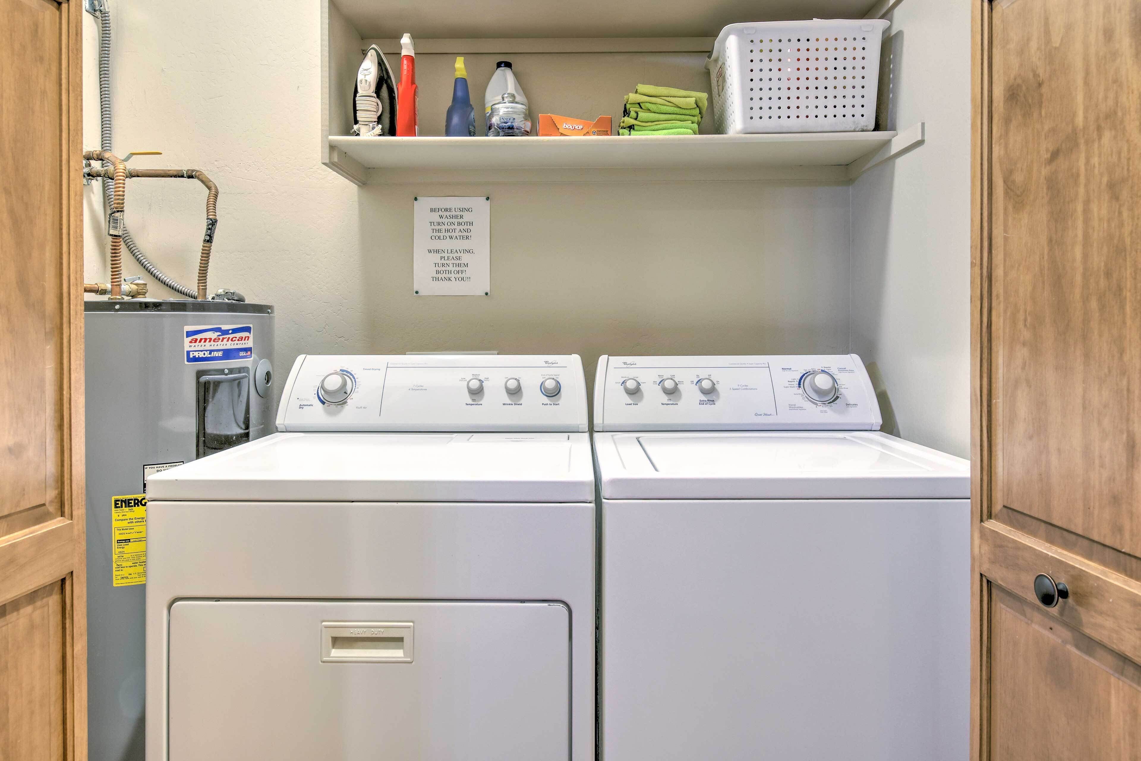 A laundry room with two stacked washers and dryers, a water heater, and a shelf with cleaning supplies.