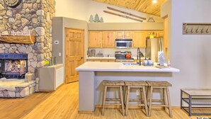 A kitchen with wooden cabinets, a stone wall, a fireplace, and a large island with stools. - Torreon Cabin Escape - Relax, Recharge and Explore (Show Low)