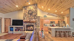 A cozy living room with a stone fireplace, a leather couch, and a flat-screen TV. - Torreon Cabin Escape - Relax, Recharge and Explore (Show Low)