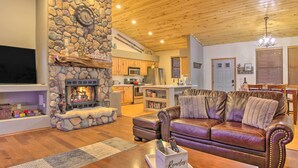 A cozy living room with a stone fireplace, leather sofa, and a television. - Torreon Cabin Escape - Relax, Recharge and Explore (Show Low)