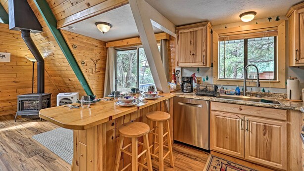 Une cabane en bois dotée d’une cuisine comprenant un coin bar, des tabourets en bois, une cuisinière et un lave-vaisselle.