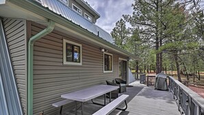 Une terrasse en bois avec une table de pique-nique et des chaises, un barbecue couvert et une rambarde en métal.