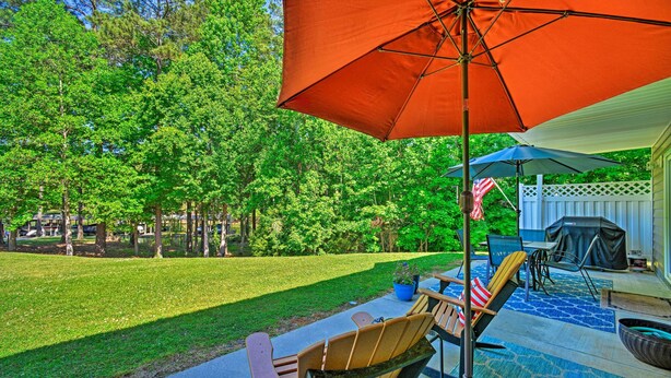 An outdoor patio with a blue umbrella, wooden chairs, and a grill area.