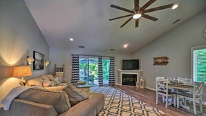 A living room with a sofa, a patterned rug, a dining table with chairs, a ceiling fan, and a fireplace.