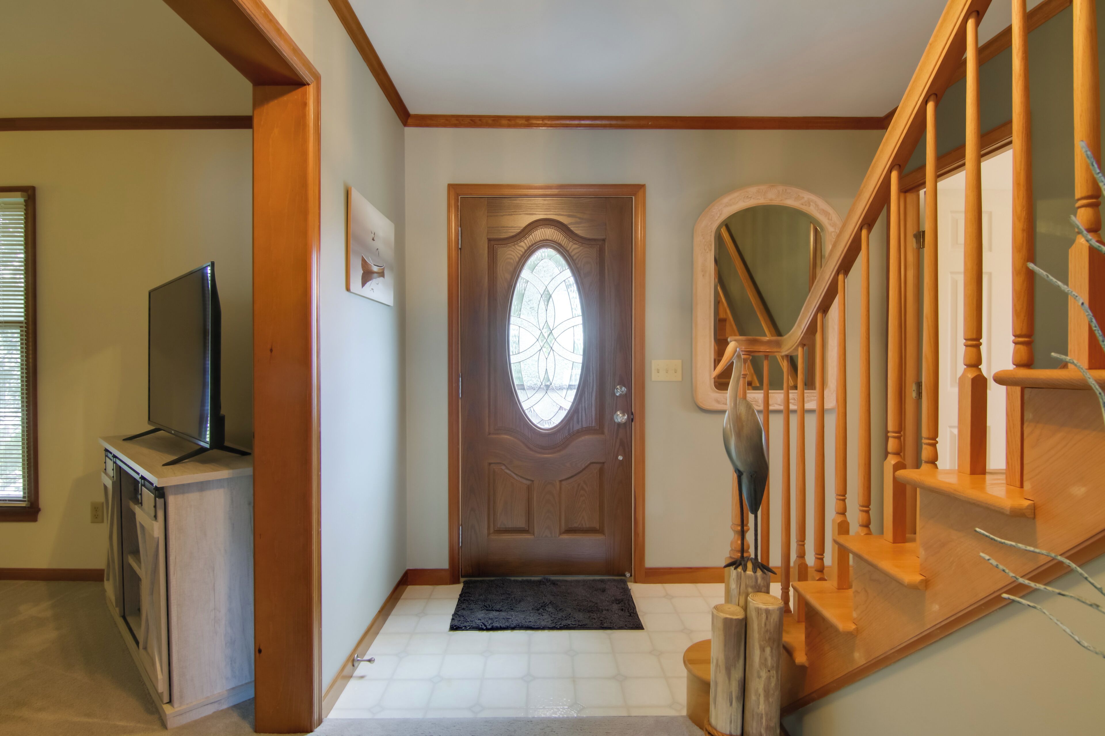 A hallway with a wooden staircase, a door with a stained glass window, and a small wooden table with a television.