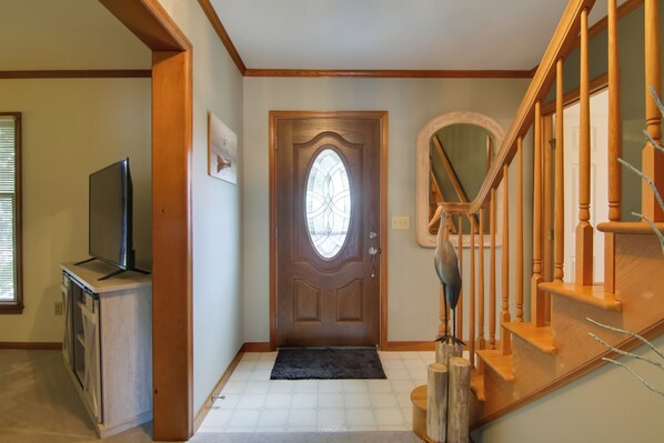 A hallway with a wooden staircase, a door with a stained glass window, and a small wooden table with a television.