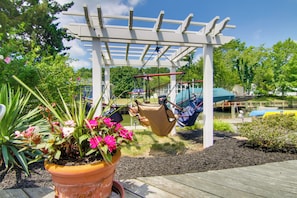 A wooden deck with a hanging swing set, a potted plant with pink flowers, and a white pergola structure.