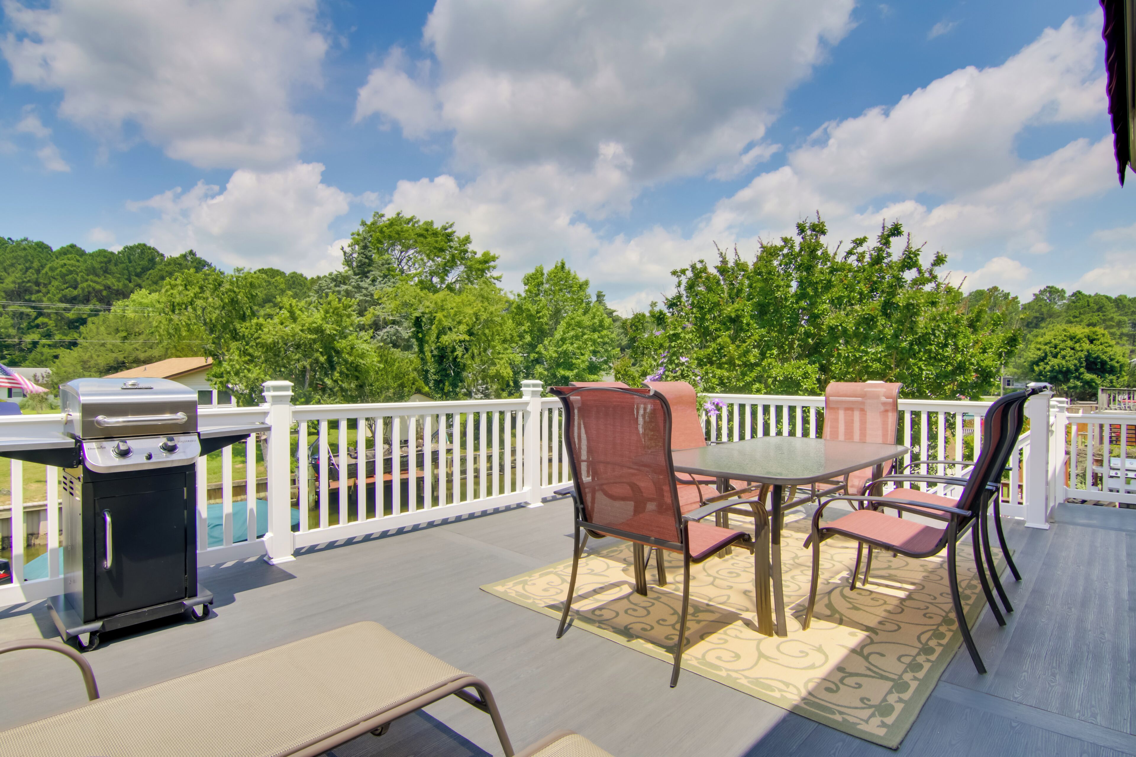 An outdoor deck with a grill, a table with chairs, and a view of a forested area.