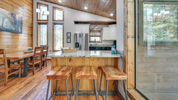 A wooden interior with a dining area, kitchen, and bar stools. - Furnished Deck, Hot Tub! Family Gem in Broken Bow (Broken Bow)