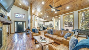 A spacious living room with a fireplace, leather sofas, a coffee table, and a large window offering a view of the outdoors. - Furnished Deck, Hot Tub! Family Gem in Broken Bow (Broken Bow)