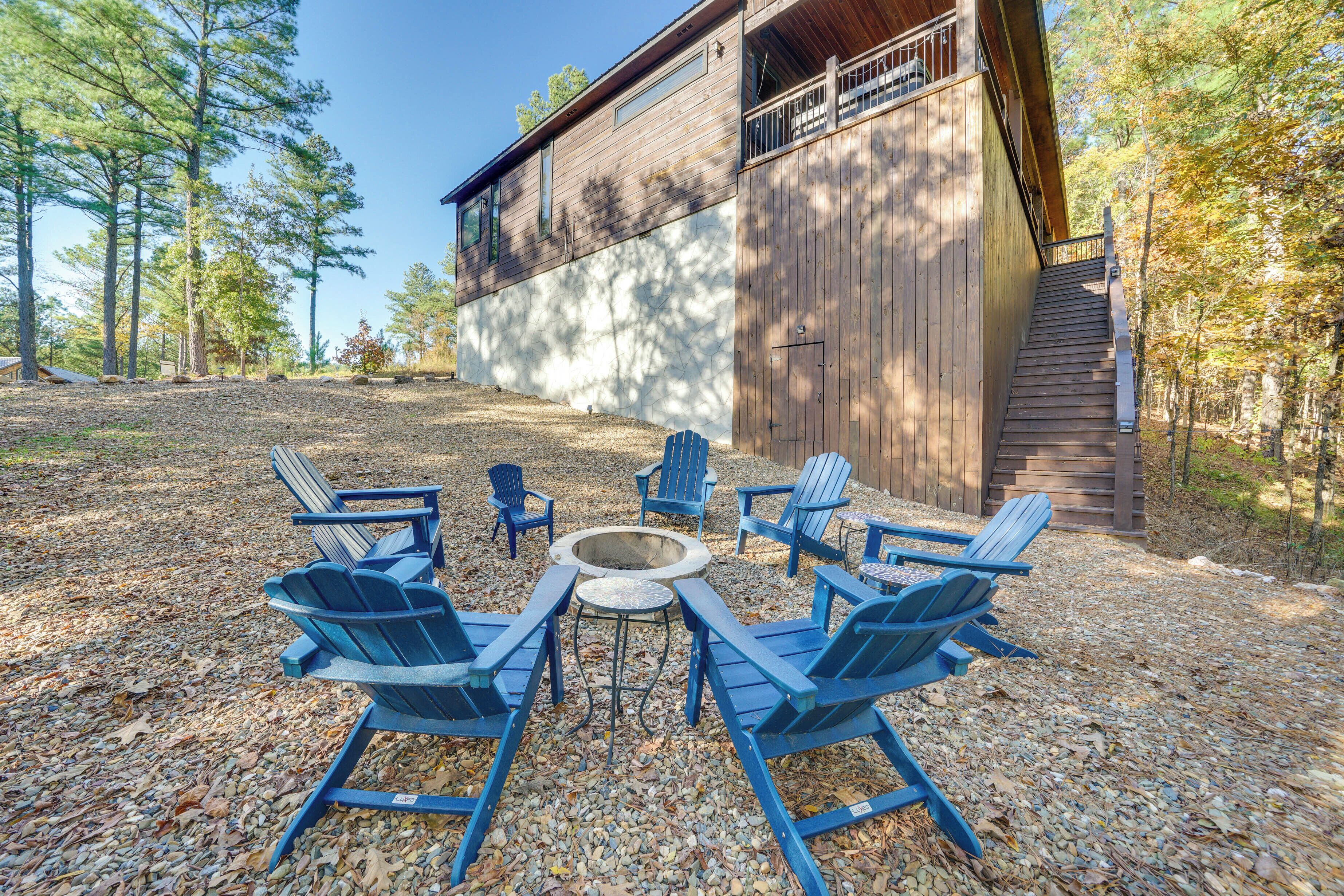 Une cabane en bois avec une cheminée en pierre et des fauteuils Adirondack bleus disposés autour.