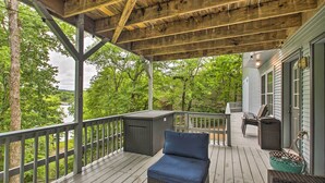A covered deck with wicker furniture, a view of a lake, and a house in the background. - Kayaks & Boat Dock: Lakeside Hot Springs Retreat (Hot Springs Village)