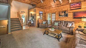 A log cabin interior with a staircase, leather couches, a wooden coffee table, and mounted animal heads on the ceiling. - Kayaks & Boat Dock: Lakeside Hot Springs Retreat (Hot Springs Village)