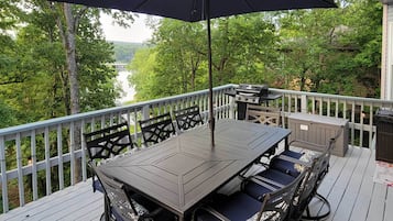 A deck with a table and chairs, a grill, and a view of a lake and trees.