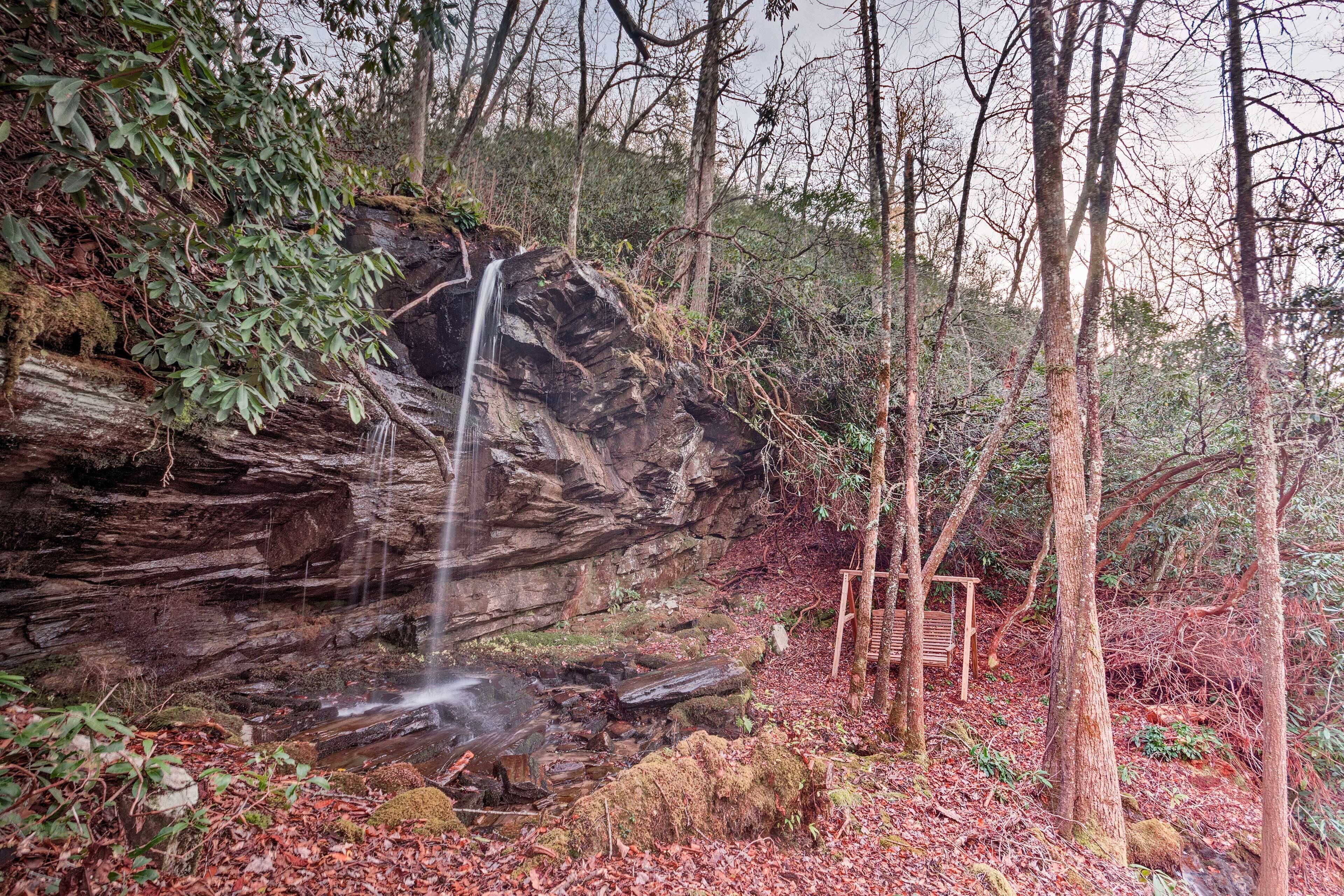 A natural rock formation with a waterfall and a wooden bench.